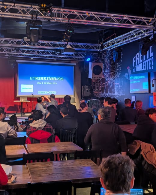 A photograph showing a group of people gathered in a dimly lit indoor venue for an 'AI Tinkerers' event, with a large screen at the front displaying event information.