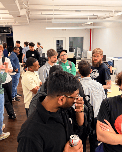 A group of people are gathered in a modern office space for a social or networking event, with many engaged in conversations.