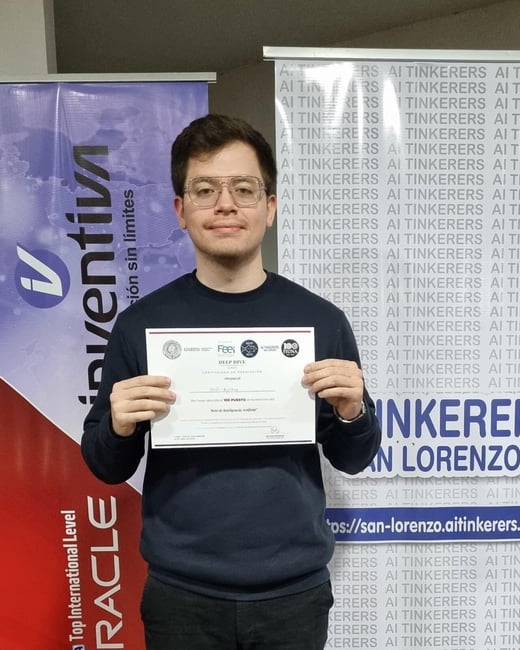 A young man stands proudly holding a certificate of achievement in front of two promotional banners at an event.