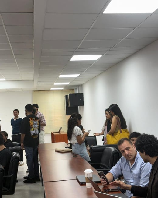An indoor photograph showing a group of people gathered in a conference room with long tables and office lighting.