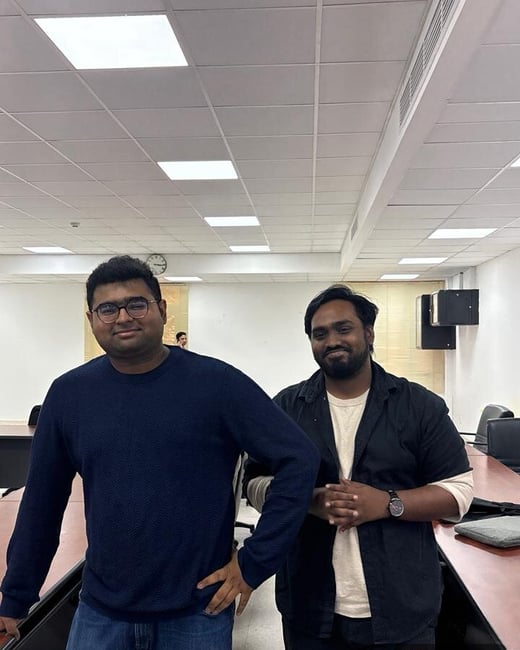 Two men stand side-by-side posing for a photo in an office conference room, with a GPS location overlay at the bottom.