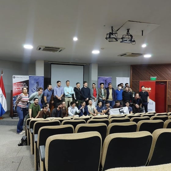 A large group of people posing for a commemorative photo on a stage in an auditorium, surrounded by event banners.