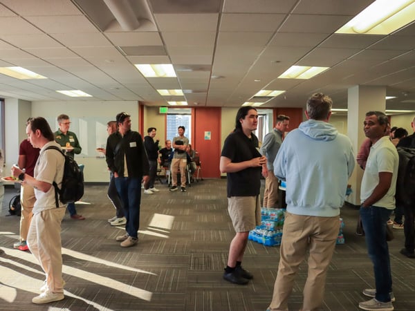 A group of people are gathered in a large, open office space, socializing and eating during an event.