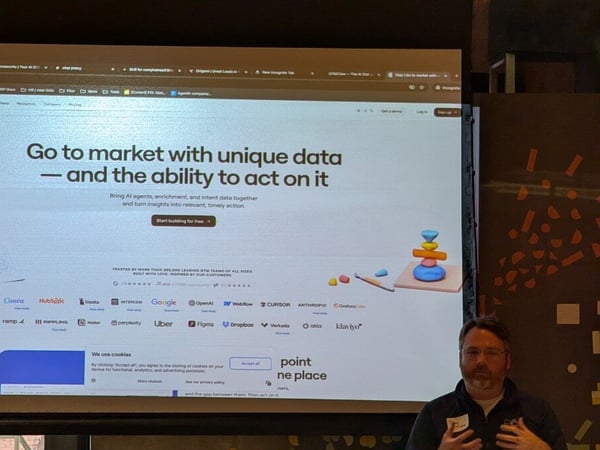 A man is giving a presentation in front of a large projector screen displaying the homepage of the website clay.com.