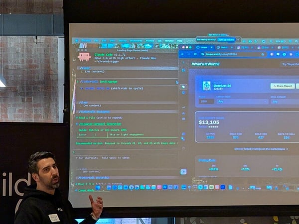 A man is giving a presentation in front of a large projection screen that displays a computer desktop with coding tools and a watch valuation dashboard.