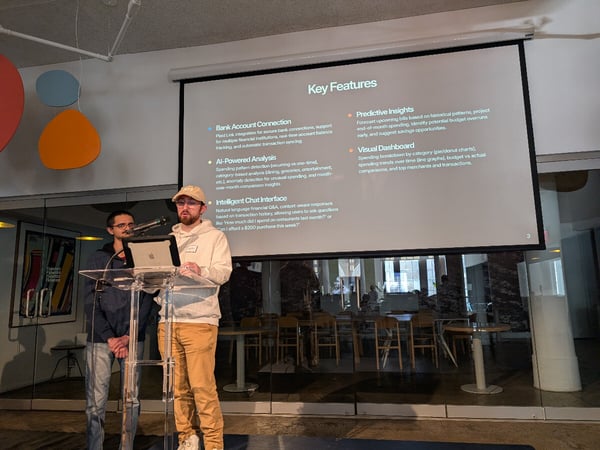 Two men are giving a presentation indoors, standing at a clear acrylic podium in front of a projection screen displaying a slide titled "Key Features" related to financial software capabilities.