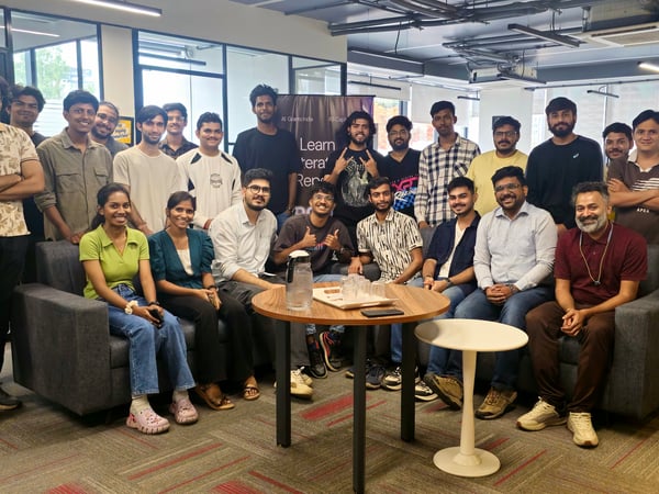 A group of approximately 25 young professionals, mostly men, posing for a group photo in a modern office setting.
