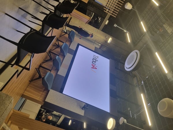 A modern office or event space featuring a large projection screen displaying 'Tribu IA' and rows of contemporary seating.
