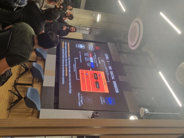 A photograph of a presentation taking place in a modern indoor setting, featuring a speaker explaining a slide titled 'LEVEL 1 - THE SOCIAL DUNGEON' to an audience.