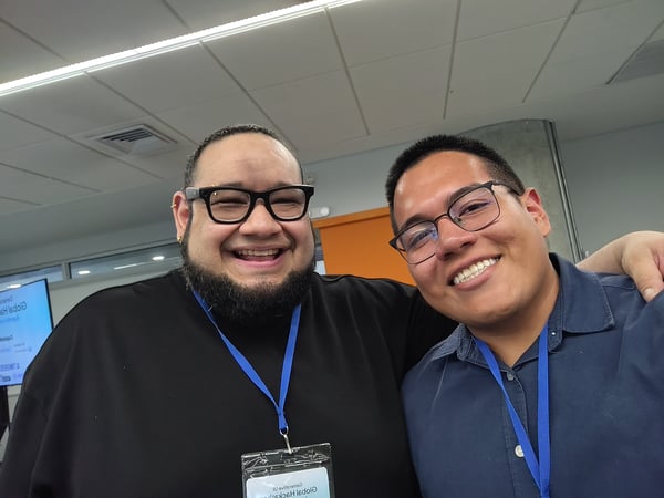 A selfie of two men smiling at an indoor event, both wearing blue lanyards.