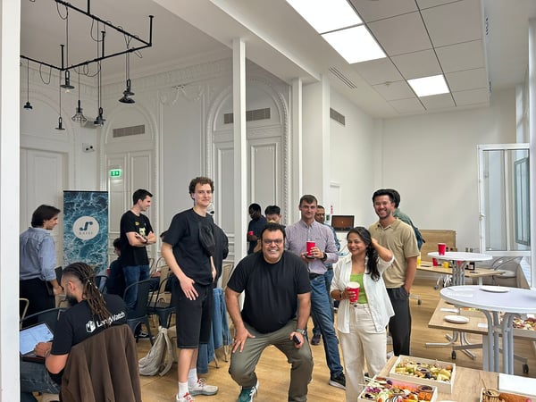 A group of people socializing and posing for a photo during an indoor event or gathering in a bright, high-ceilinged room featuring ornate white walls and modern furniture.