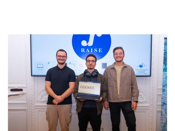 Three young men stand side-by-side in a formal meeting room, posing in front of a large screen that displays the 'RAISE' logo and company contact information. The man in the center holds a small laptop with the word 'COOKED' visible on the screen.