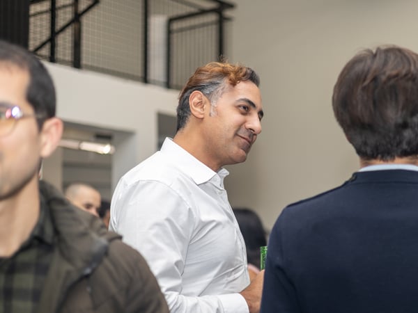 A candid photograph of several people socializing in a modern indoor setting, with a man in a white shirt as the central focus.