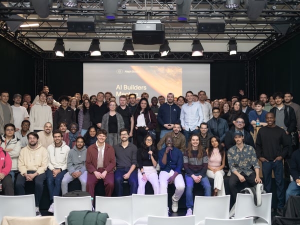 A large group of people are posing for a group photograph on a stage at an 'AI Builders Meetup' event hosted by Aleph Studios.