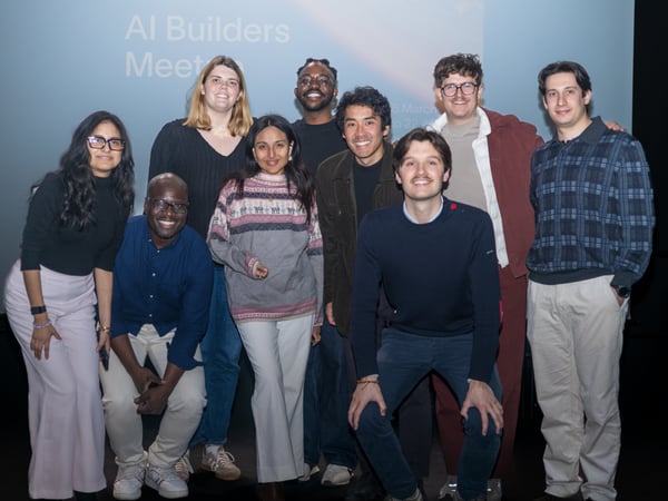 A group of nine diverse individuals posing for a group photo in front of a presentation screen at an event.