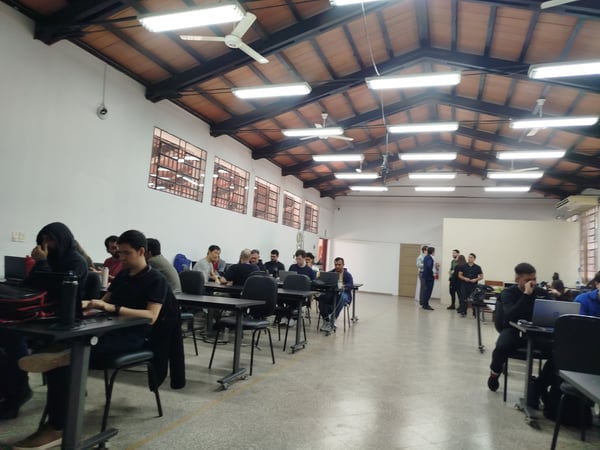 A wide-angle shot of people working on laptops in a large indoor room with a high, vaulted wooden ceiling and fluorescent lights.