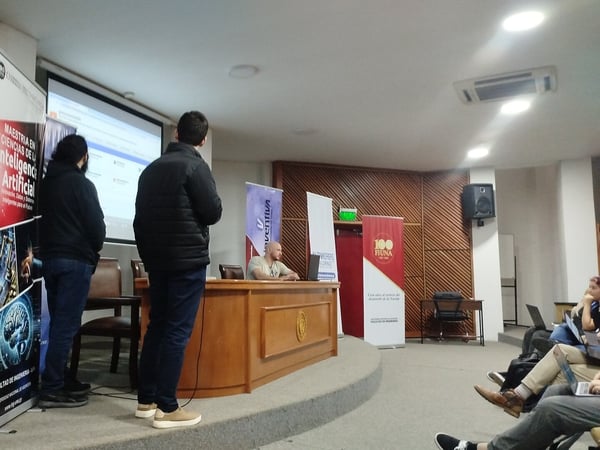 A presentation or academic event taking place in an auditorium, featuring speakers on stage next to banners and a Paraguayan flag.