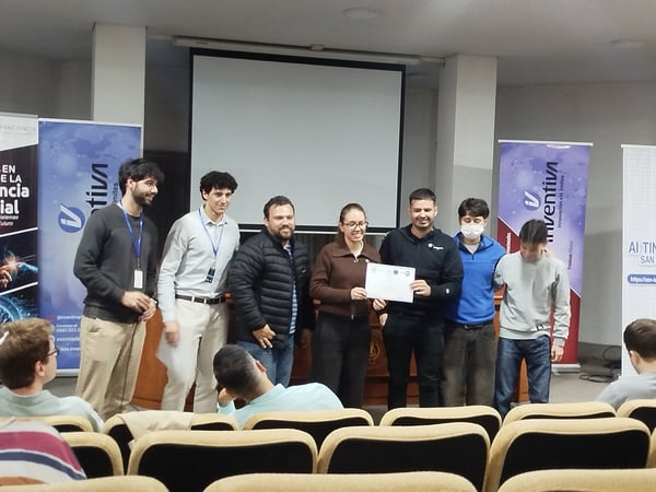 A group of people standing on a stage or in front of a room, holding a certificate during an award ceremony or presentation.