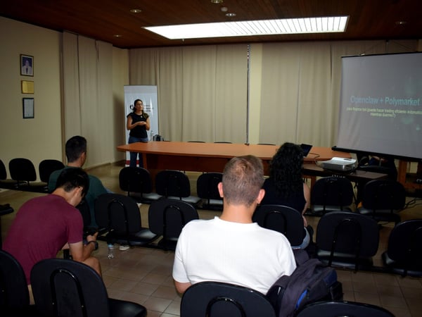 A woman is giving a presentation in a meeting room with a projector screen showing text in Spanish to a small audience.