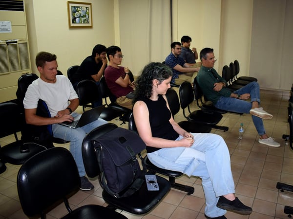 A group of people are seated in a lecture-style room, attentively looking towards the side as if watching a presentation or talk.
