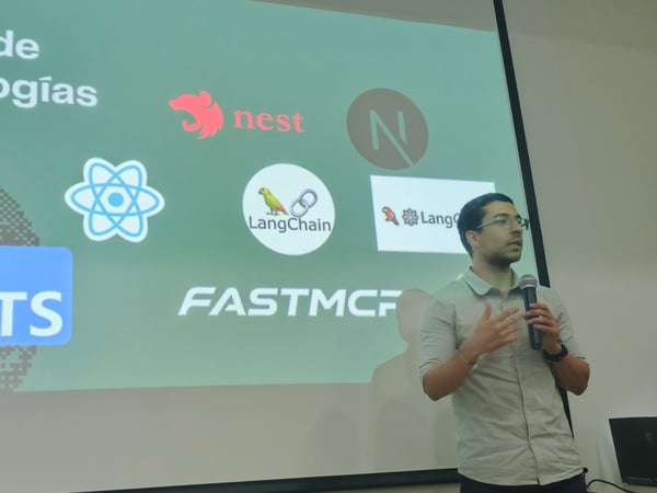 A man is giving a presentation in front of a projected slide titled 'Stack de tecnologías', which displays various software logos like Python, React, and LangChain.