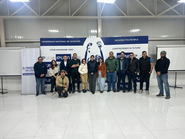 A group photo of thirteen people standing in front of a blue and white university backdrop inside a large hall.