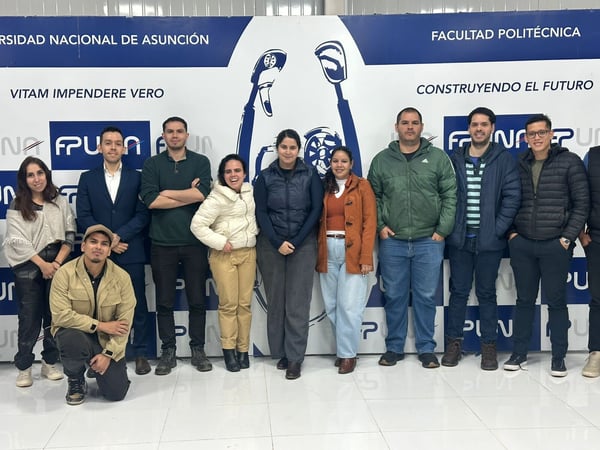 A group of eleven people posing for a group photo in front of a blue and white banner for the Universidad Nacional de Asunción.