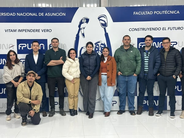 A group of ten people posing for a group photo indoors in front of a blue and white banner for the Universidad Nacional de Asunción.
