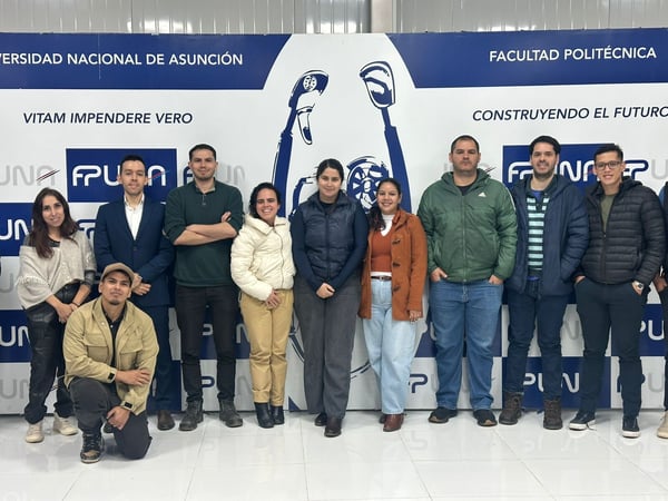 A group of ten people posing for a group photo indoors in front of a blue and white banner for the Universidad Nacional de Asunción.