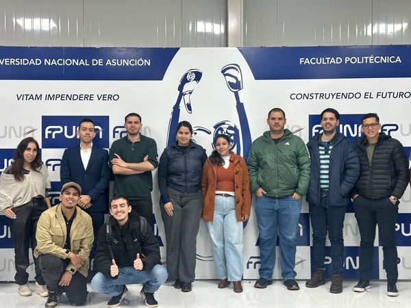 A group photo of ten individuals posing in front of a blue and white banner for the Universidad Nacional de Asunción's Facultad Politécnica.
