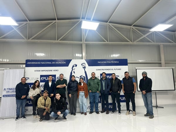 A group photo of thirteen people posing in front of a blue and white banner for the Universidad Nacional de Asunción, Facultad Politécnica.