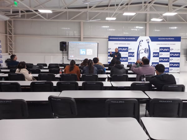 A presentation taking place in a university classroom, with a speaker standing at the front near a screen and a small audience seated at desks.