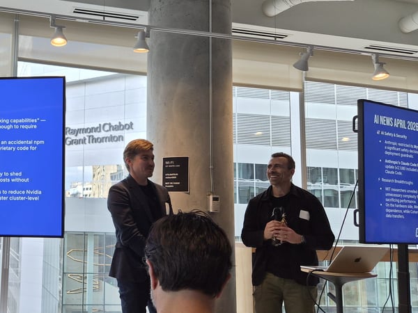 Two men are presenting at an AI Tinkerers event in Montreal, standing next to a large screen displaying AI-related news headlines dated April 2026.