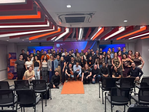 A large group of people posing for a group photo in a modern office or event space with a distinctive orange and white ceiling design.