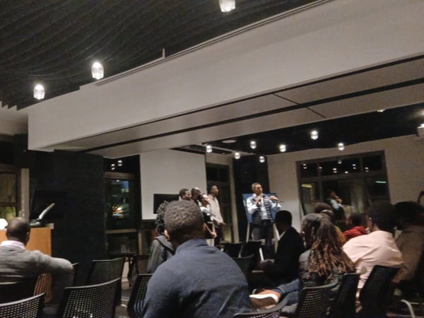 An indoor photograph capturing an audience seated in a modern auditorium watching a presentation or panel discussion.
