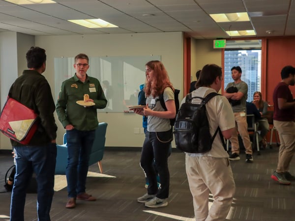 A group of people are socializing and networking in an office setting, with some individuals holding plates of food and drinks.