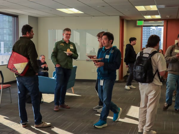 A group of people are socializing and eating in an office common area during a networking event.