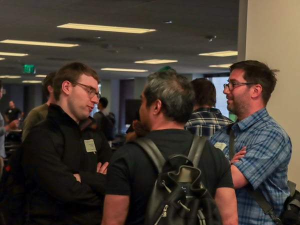 A group of men are engaged in a conversation during an indoor networking event or social gathering.