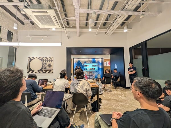 A candid photograph capturing a group of people attending a meeting or presentation in a modern office space featuring an exposed ceiling and minimalist decor.
