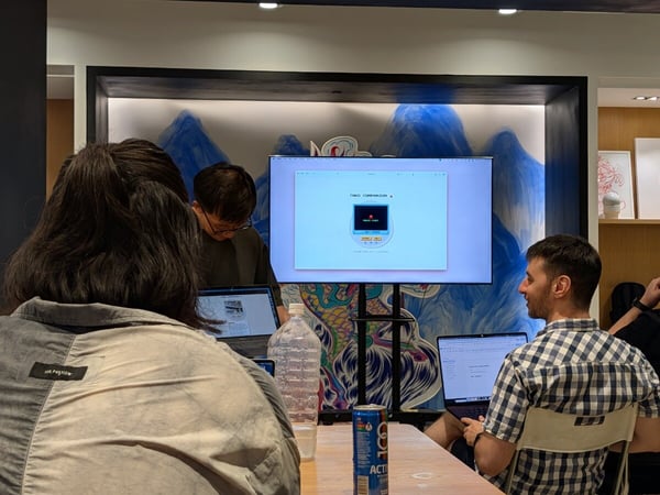 A photograph capturing an indoor meeting or workshop where several people are seated around a table, viewing a presentation on a large monitor displaying a software interface labeled 'Tingo Companion.'
