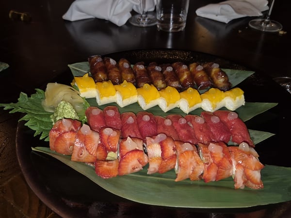 A large platter of assorted sushi and rolls, featuring unique toppings like strawberries and mango, served on a dark table in a restaurant.