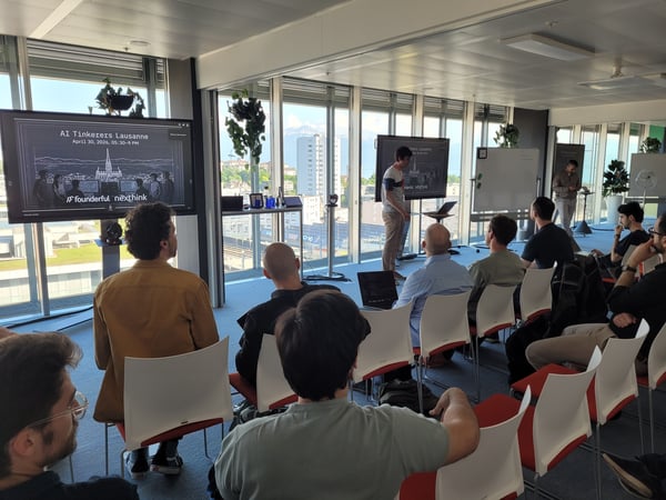 A group of people are attending a presentation titled 'AI Tinkerers Lausanne' in a modern office space with large windows overlooking a cityscape.