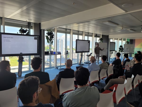 A man gives a presentation to a seated audience in a modern office with large windows overlooking a city.