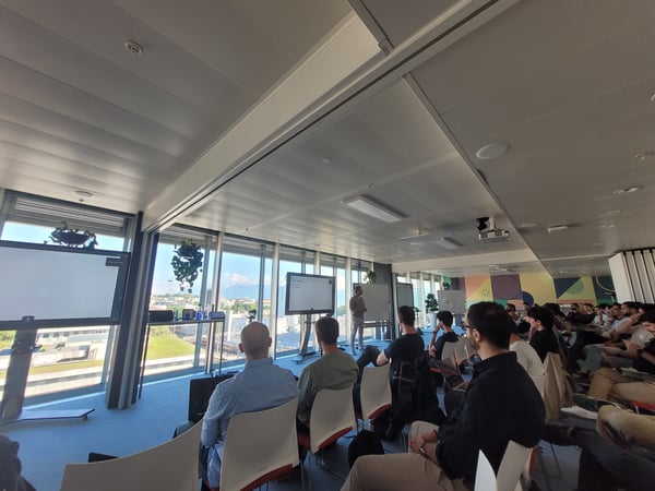 A group of people attending a presentation in a modern office with large windows overlooking a city.