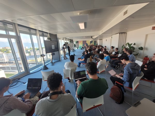 A group of people attending a technical presentation or workshop in a modern office with large windows overlooking a city.