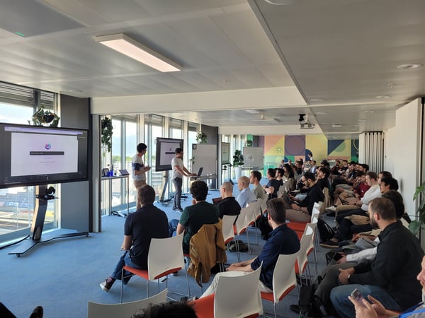 A group of people in a modern office setting attending a presentation or demonstration featuring large digital displays and a whiteboard.