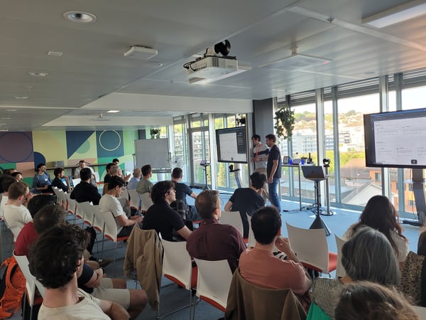 A group of people attending a presentation or product demo in a modern office space with large windows overlooking a city.