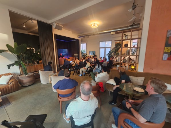 An indoor photograph of a presentation or talk being held in a modern, stylishly decorated lounge space, with an audience seated in chairs facing a speaker on a small stage.