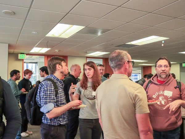 A group of people are socializing and networking in an office setting, with some individuals holding plates of food.