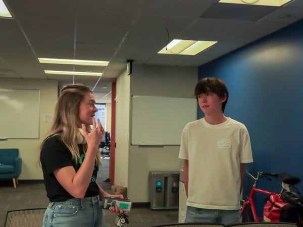 A woman and a young person are standing in an office hallway, engaged in a conversation.